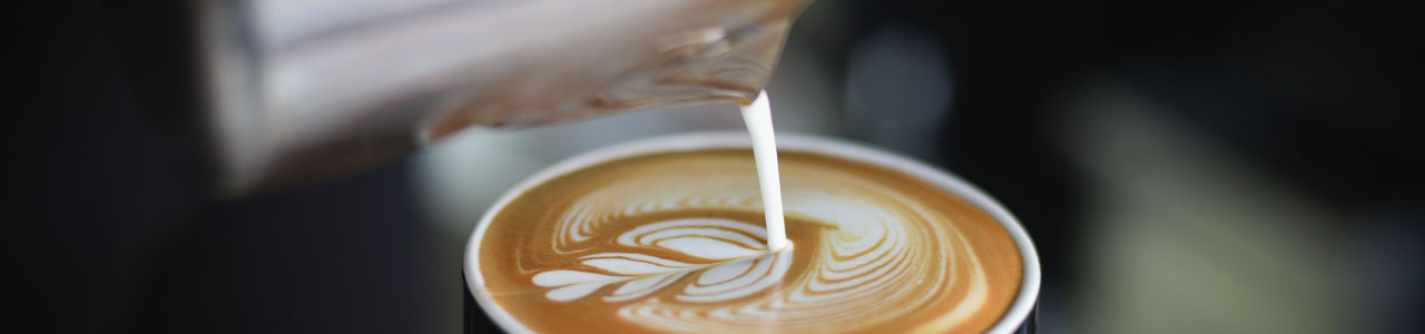 Leite sendo despejado em uma xícara de café, de forma a formar uma imagem de três corações.