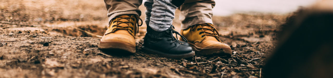 Imagem mostra apenas os sapatos de duas pessoas. Os pés maiores, indicando serem os do pai, e entre eles dois pés menores, indicando serem os do filho.