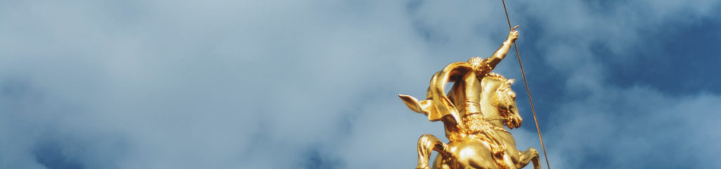 imagem de uma estatua dourada comemorando vitória. Um homem está em cima de um cavalo com os braços erguidos.