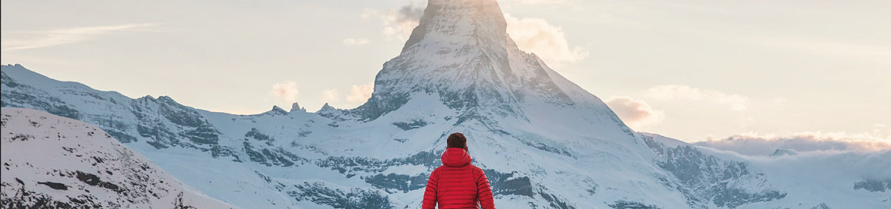 imagem mostra um homem observando uma montanha coberta de gelo ao longe.