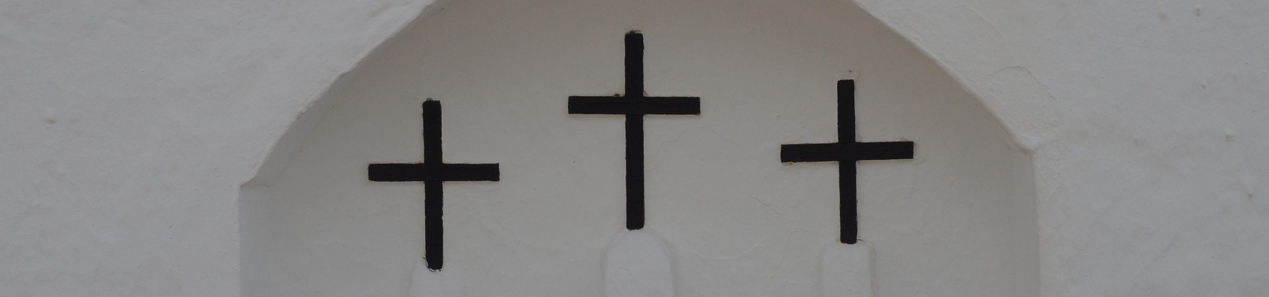 Imagem de três cruzes pretas sobre uma parede branca.