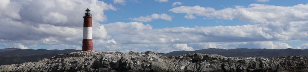 Imagem de um farol sobre uma formação de rochas. No fundo, pode-se ver um céu com algumas nuvens.