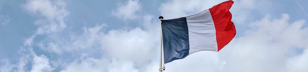 Imagem da bandeira da França. Ao fundo, um céu azul com nuvens.