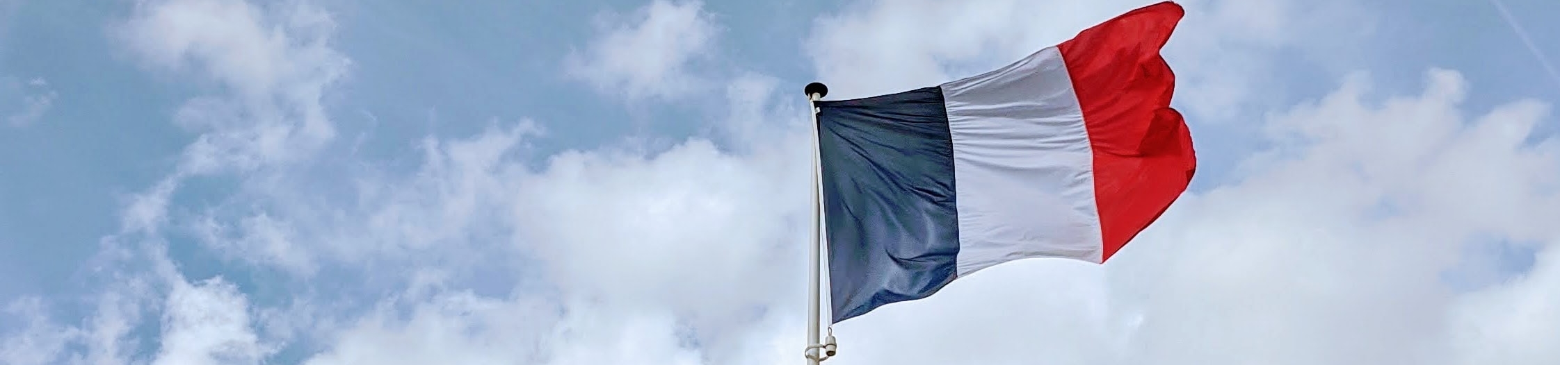 Imagem da bandeira da França. Ao fundo, um céu azul com nuvens.