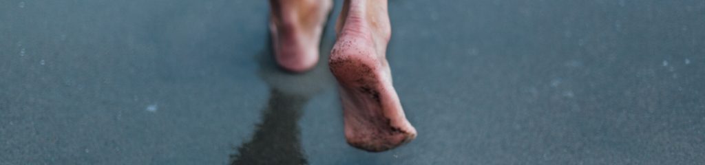 Imagem dos pés de uma pessoa, que caminha sobre a areia.