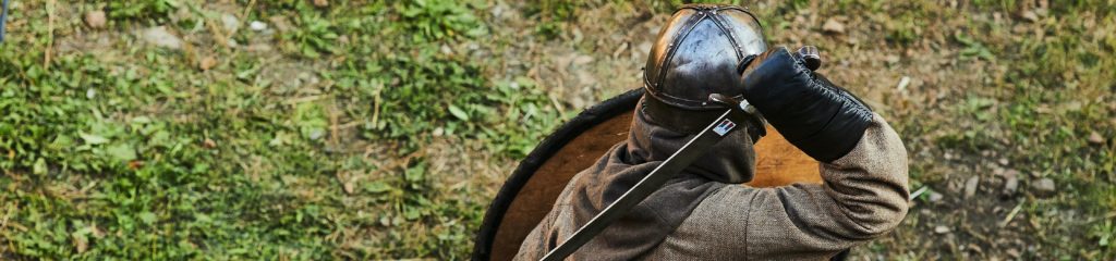 Uma pessoa veste roupa de guerreiro. Ela segura uma espada e um escudo.