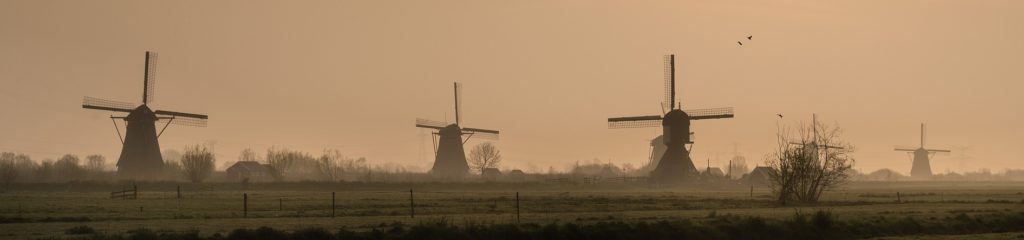 Imagem de vários moinhos de vento no horizonte, sob um céu alaranjado.