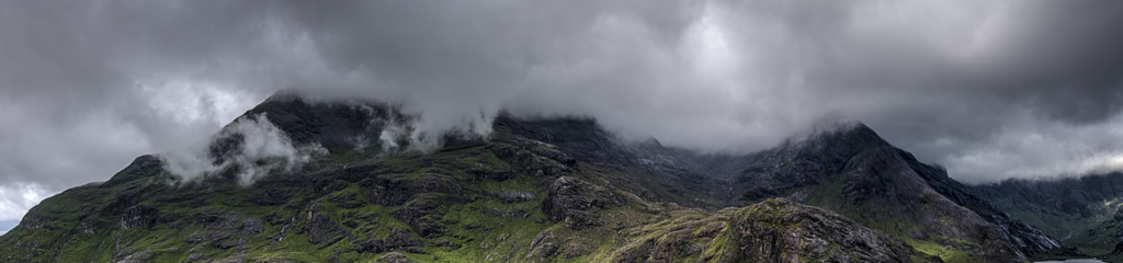 Imagem de montanhas cobertas por grama. Acima delas, pode-se ver um céu nublado.