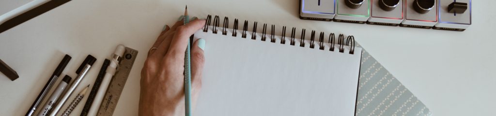 Uma pessoa segura um lápis com a mão esquerda, apoiada em um caderno.