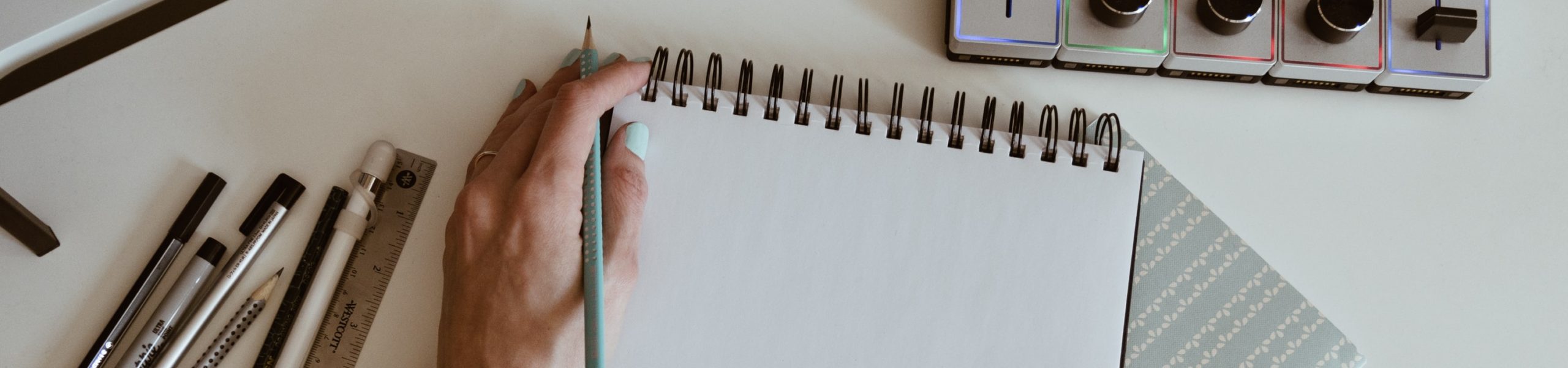 Uma pessoa segura um lápis com a mão esquerda, apoiada em um caderno.