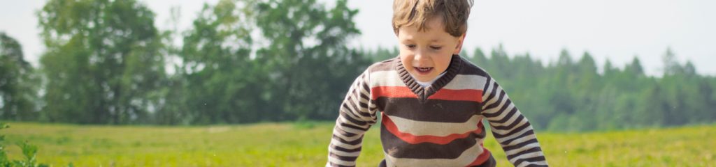 Imagem de um menino brincando em um gramado.