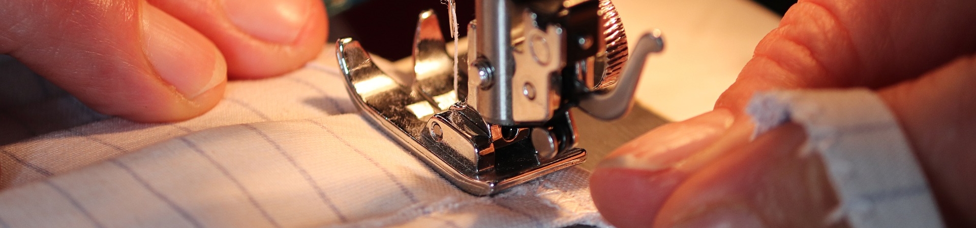 Detalhe das mãos de uma pessoa utilizando uma máquina de costura.