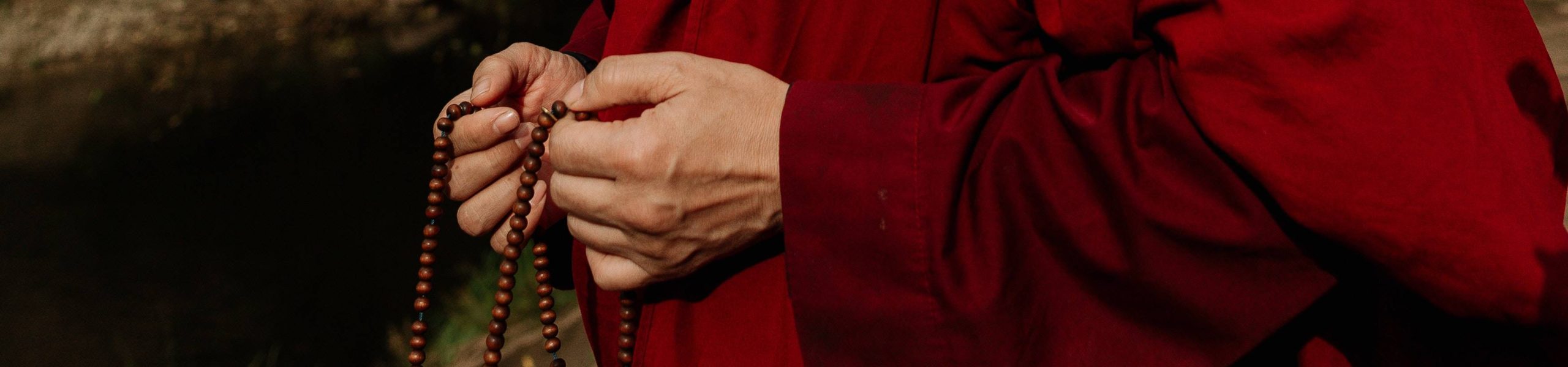 Monge com uma túnica vermelha segurando um terço com as duas mãos.