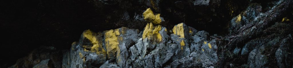Imagem do interior de uma caverna, onde se vê um parede de pedras com tons amarelados.