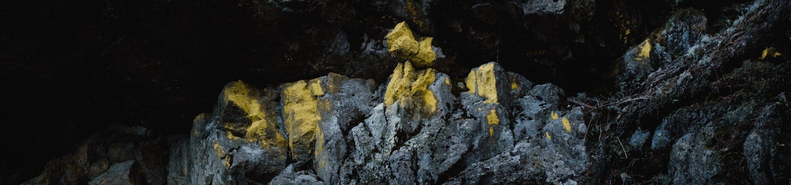 Imagem do interior de uma caverna, onde se vê um parede de pedras com tons amarelados.