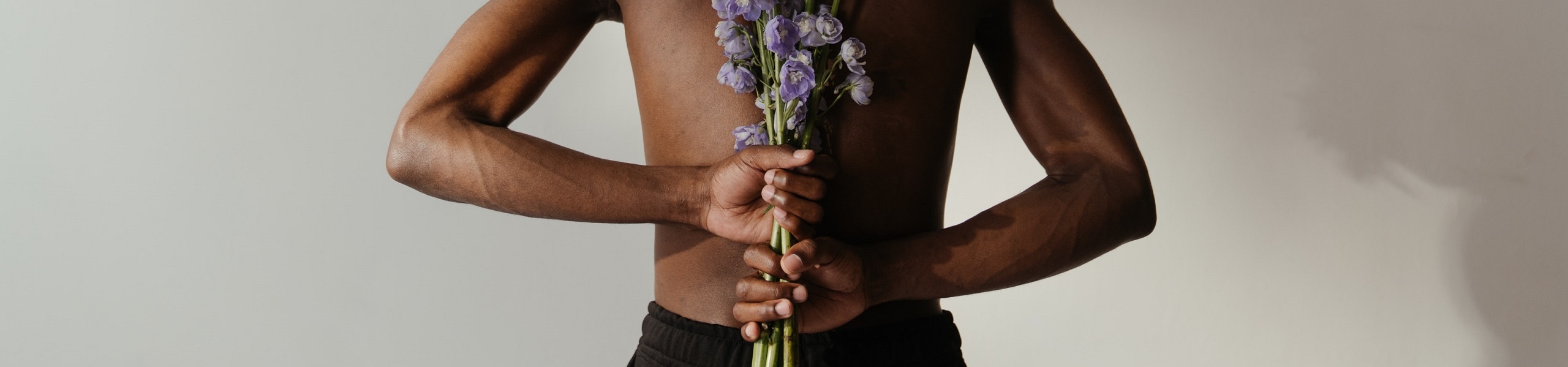 Homem de costas segurando uma planta do gênero delfínio